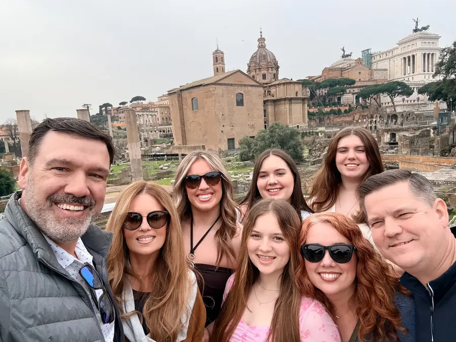 A group of travelers smiling together at the Roman Forum in Rome